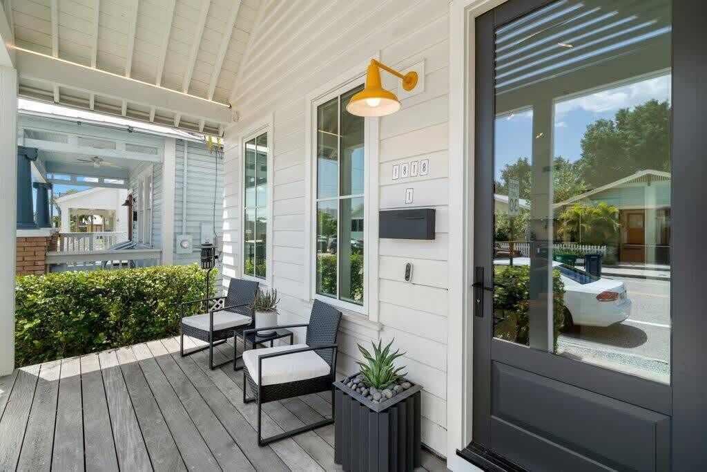 A covered porch with outdoor seating, a large window, and a door with a number plate.