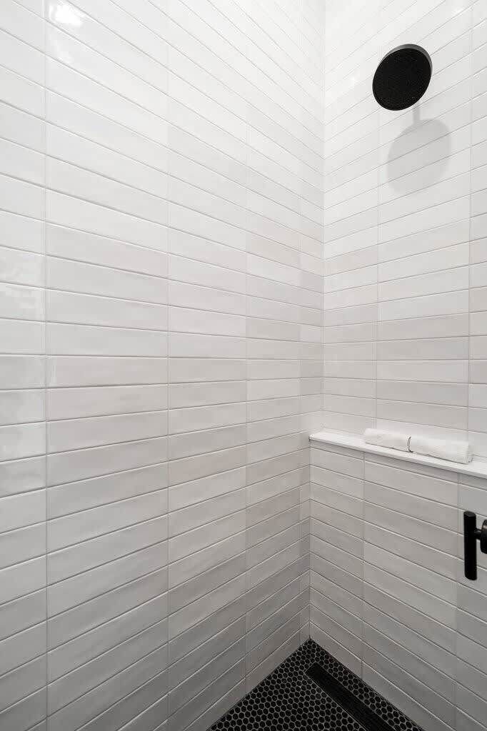 Een badkamer met witte betegelde wanden en een zwarte afvoer.