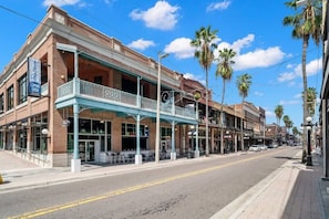 A street view with a building featuring a balcony and storefronts.