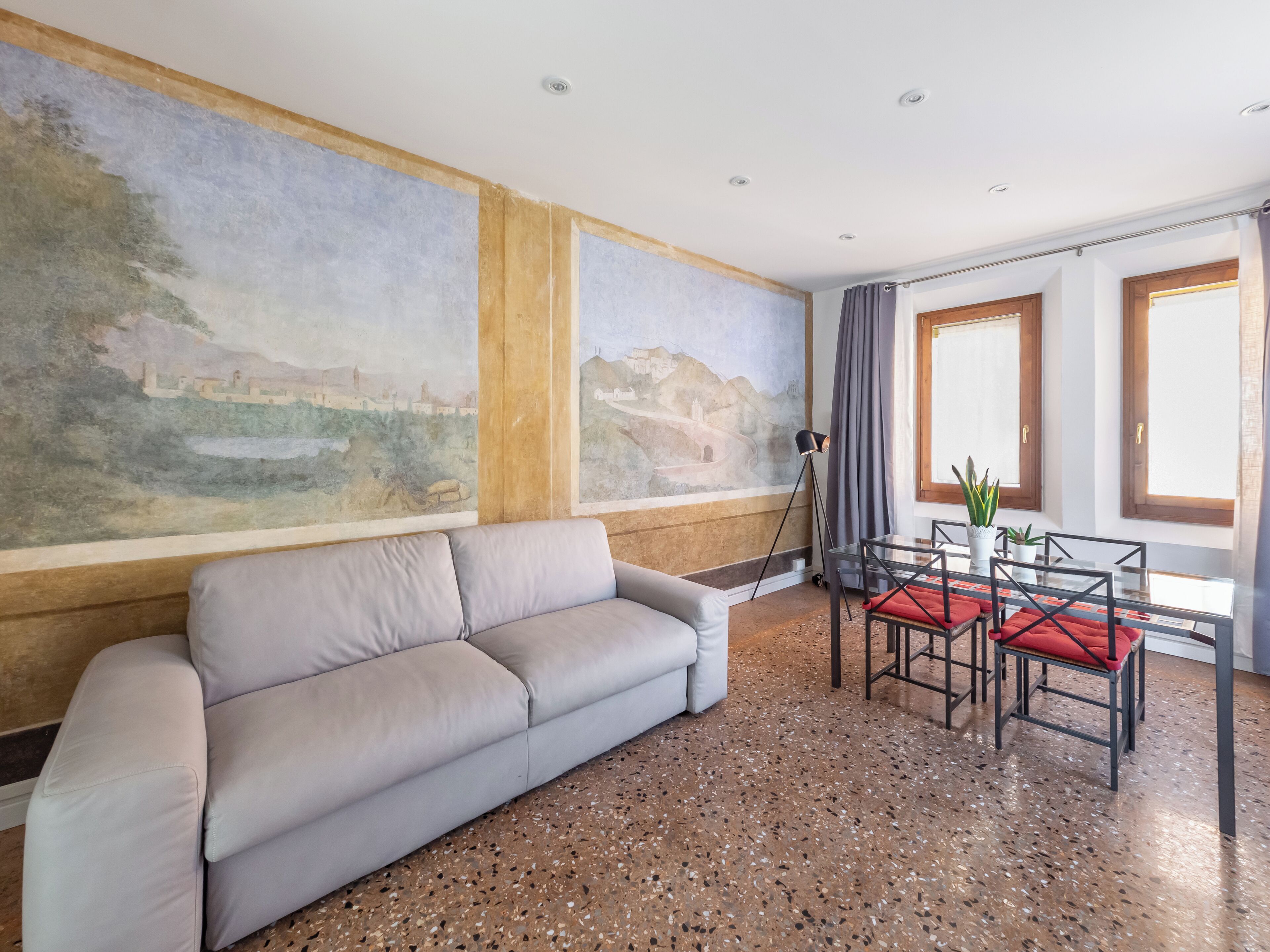 Un salon moderne comprenant un canapé, une table à manger avec des chaises, une lampe sur pied et une grande fresque murale.