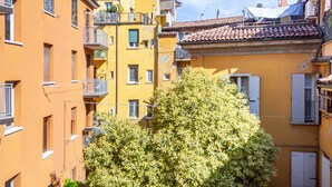 A narrow street with yellow buildings, balconies, and a tree in the foreground. - Casa Picta (Bologna)