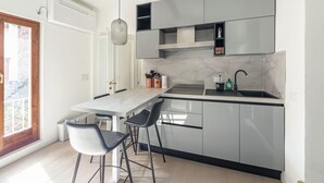 A modern kitchen with a marble countertop, grey cabinets, a built-in sink, and a pendant light. - Casa Picta (Bologna)