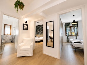 Una habitación de hotel moderna con un sillón blanco, una cama con cabecera, un espejo grande y un área de comedor con una mesa y sillas.