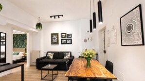 Ett modernt vardagsrum med en matplats, en svart soffa, ett matbord i trä och ett konstverk med svart ram på väggen.