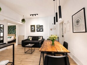 Ein modernes Wohnzimmer mit Essbereich, einer schwarzen Couch, einem Holztisch und einem Bilderrahmen in Schwarz an der Wand.