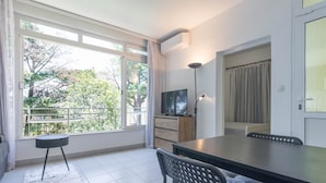 Een moderne woonkamer met een groot raam, een flatscreen-tv, een eettafel en een bank.