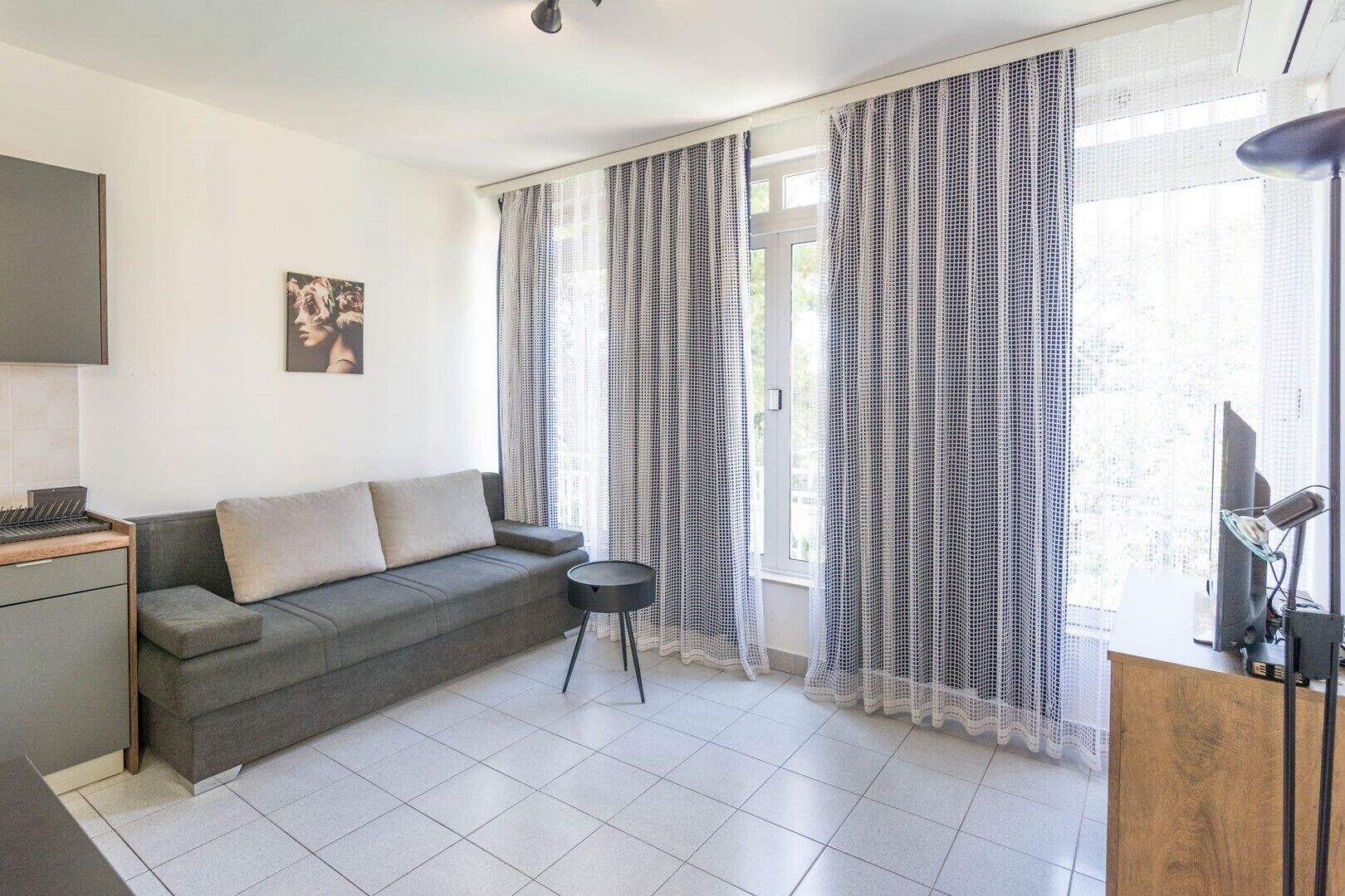 A modern living room with a grey sofa, a small round table, and a TV on a wooden stand.