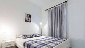 Een slaapkamer met een bed, nachtkastje, lamp, foto aan de muur en raam met gordijn.