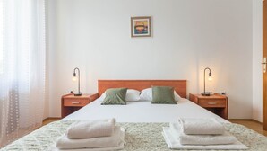 A neatly made bed with two pillows, a wooden headboard, and two bedside lamps. - Apartment Krešo with Balcony (Biograd na Moru)