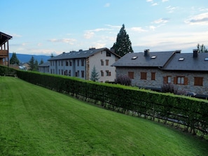 Une rangée d’immeubles résidentiels aux façades en pierre et aux toits à pignon, avec une pelouse bien entretenue et un arbuste en premier plan.