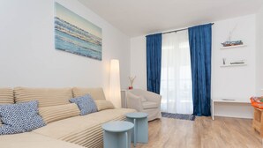 A modern living room with a sofa, two side tables, a chair, and a painting on the wall.