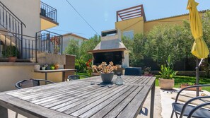 Une terrasse avec une table en bois, des chaises, un barbecue et des plantes en pot.