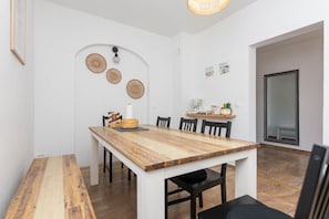 A dining area with a wooden table, chairs, a hanging light fixture, and wall-mounted decorative plates.