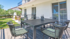 A patio with a table and chairs, a railing, and a view of a garden and buildings.