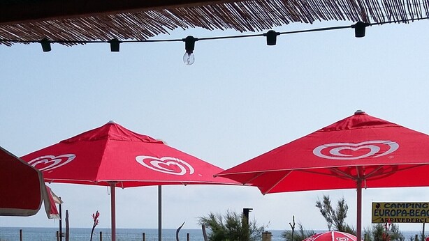 Outdoor seating with red umbrellas, a view of the beach, and a sign indicating a camping area.