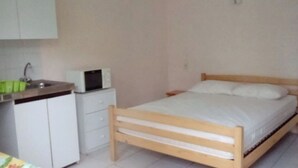 A bedroom with a wooden bed, a bedside table, a white dresser, and a microwave on top of the dresser.