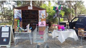 A small outdoor market stall with a sign reading "Mini Market," selling various items like hats and accessories.