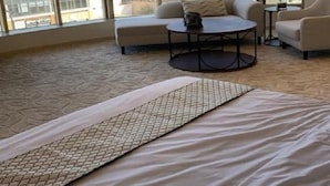 A modern hotel room with large windows, a sofa, a round coffee table, and a bed with a patterned bedspread. - The S Hotel (Jeddah)