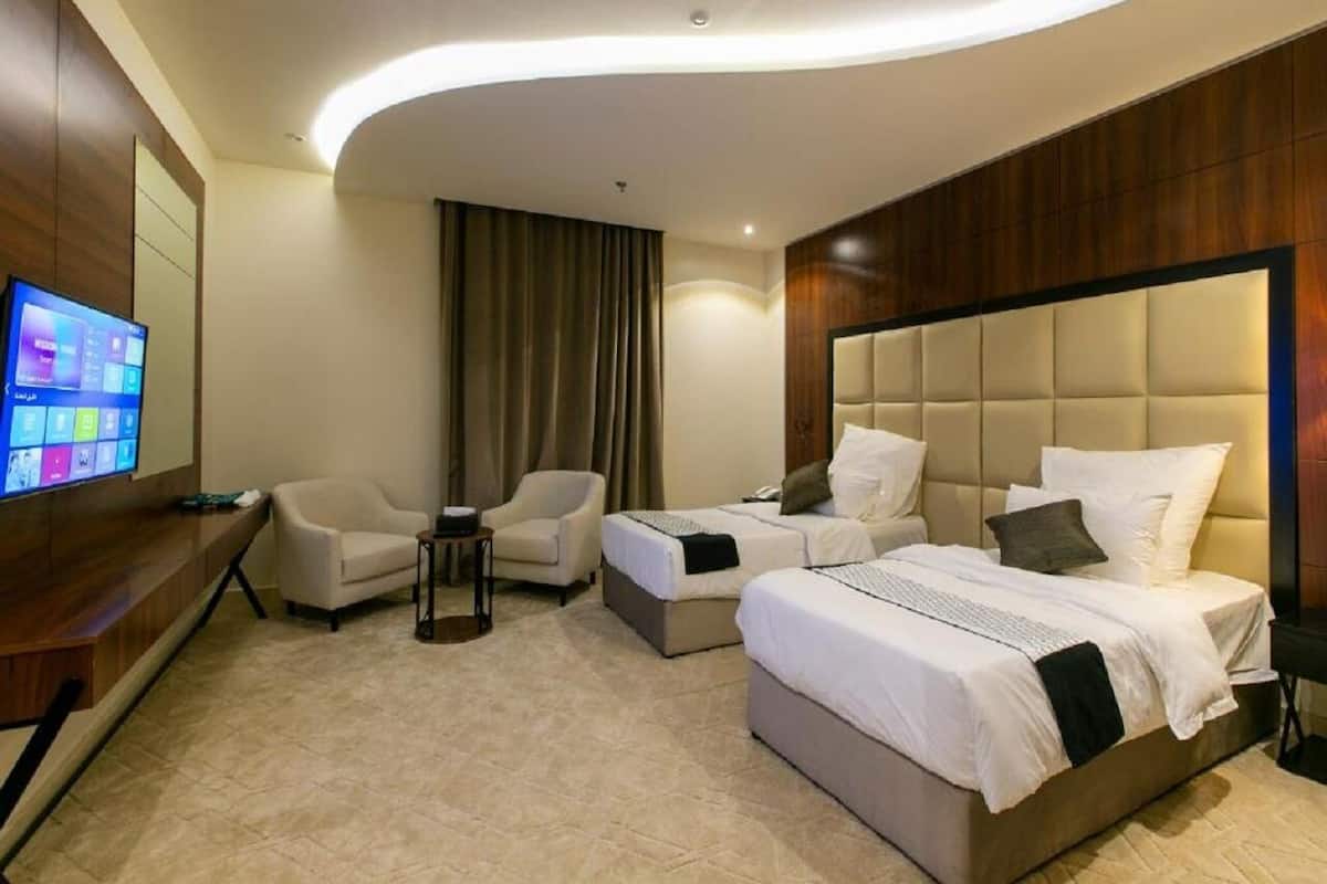 A modern hotel room with a large bed, two smaller beds, a TV, and a seating area with chairs.