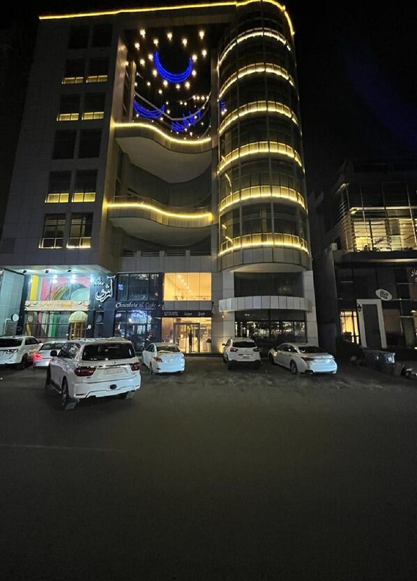 Un edificio moderno con fachada curva, varios pisos y un estacionamiento con varios coches.