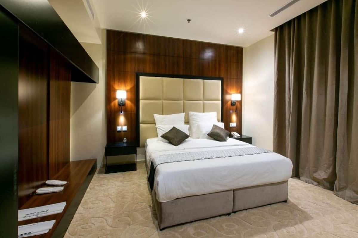 A modern hotel room with a large bed, wooden paneling, and two bedside lamps.