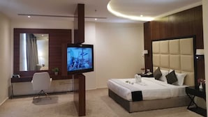 A modern hotel room with a bed, a desk, a chair, a TV, and a large mirror. - The S Hotel (Jeddah)