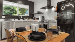 Une cuisine moderne avec un réfrigérateur noir, des appareils en acier inoxydable et une fenêtre donnant sur un espace verdoyant.