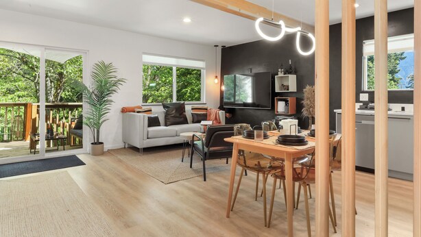 Une cuisine moderne dotée d’un grand îlot central, un coin repas avec une table et des chaises en bois, et un espace de vie avec un canapé et une grande fenêtre donnant sur un espace verdoyant.
