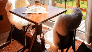Un espace repas avec une table et des chaises en bois, un lustre et une vue sur un paysage verdoyant grâce à de grandes fenêtres.