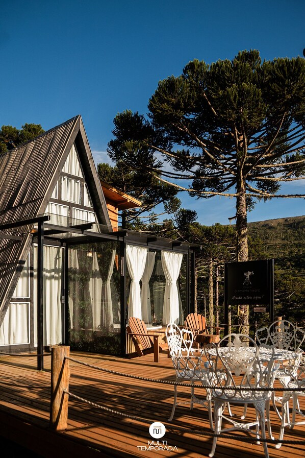 A wooden deck with outdoor furniture, a glass enclosure, and a mountain backdrop. - Chalé Diamante Negro - Urubici - SC (Urubici)