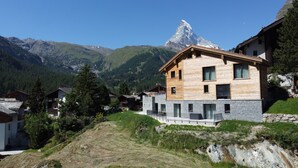 Ein modernes Holzhaus mit Steinverzierungen vor einer Berglandschaft mit schneebedecktem Gipfel.