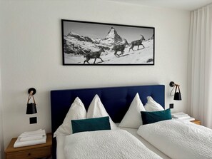 Quarto de hotel com uma cama, almofadas, mesa de cabeceira, luminária, quadro na parede e janela com cortinas.