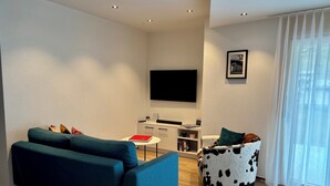 Ein modernes Wohnzimmer mit Sofa, Couchtisch, Fernseher und einem kleinen Beistelltisch.