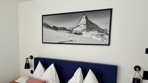 Ein Hotelzimmer mit einem großen Bett, weißen Kissen, einem blauen Kopfteil, einem gerahmten Bild einer Berglandschaft und einem Nachttisch mit einer Lampe.