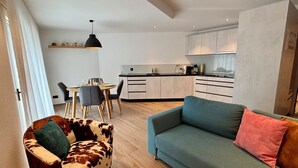 Ein modernes Wohnzimmer mit einer Couch, einem Ledersessel und einem Essbereich mit Tisch und Stühlen.