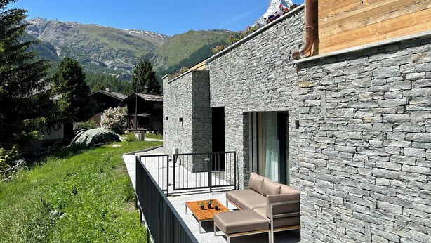 Ein modernes Gebäude aus Stein mit einem Holzaufbau und einem Balkon mit Sofa und Tisch.