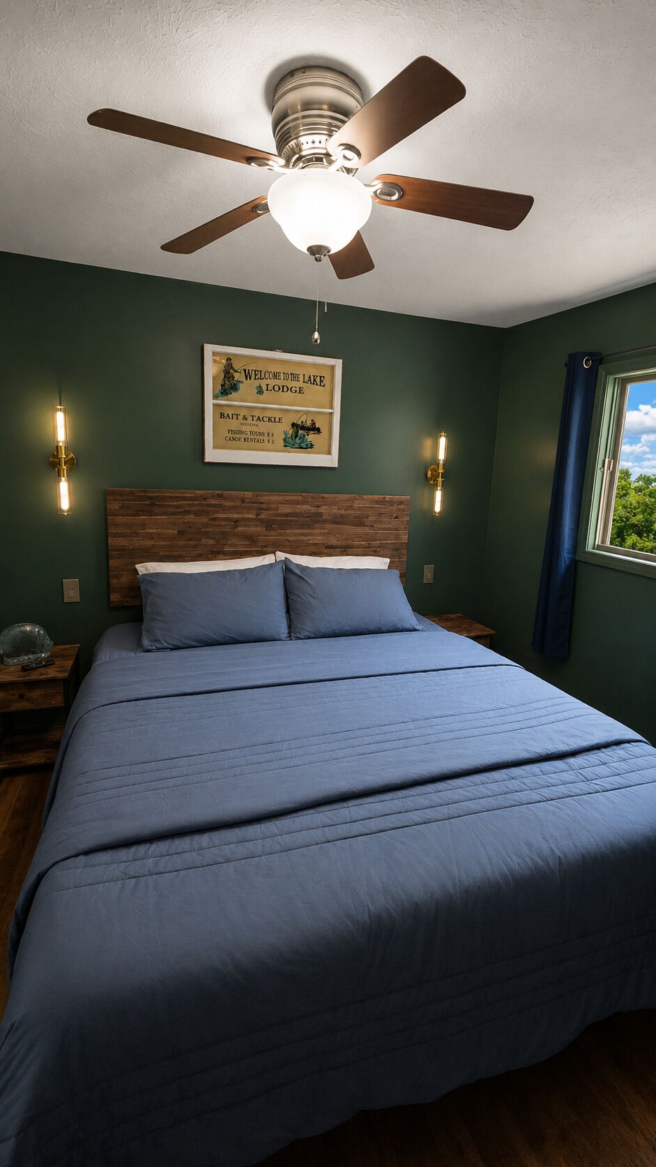 Ein Schlafzimmer mit einem Bett, Deckenventilator, Wandleuchten, einem gerahmten Willkommensschild und einem Fenster mit Blick.