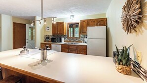 Eine moderne Küche mit Holzausstattung, einem weißen Kühlschrank und einer großen Kochinsel mit Wasserkocher und Besteck.