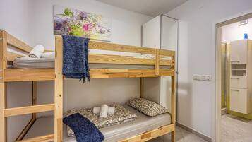 A bunk bed with a blue blanket, a floral painting, and a wardrobe in a room with white walls.