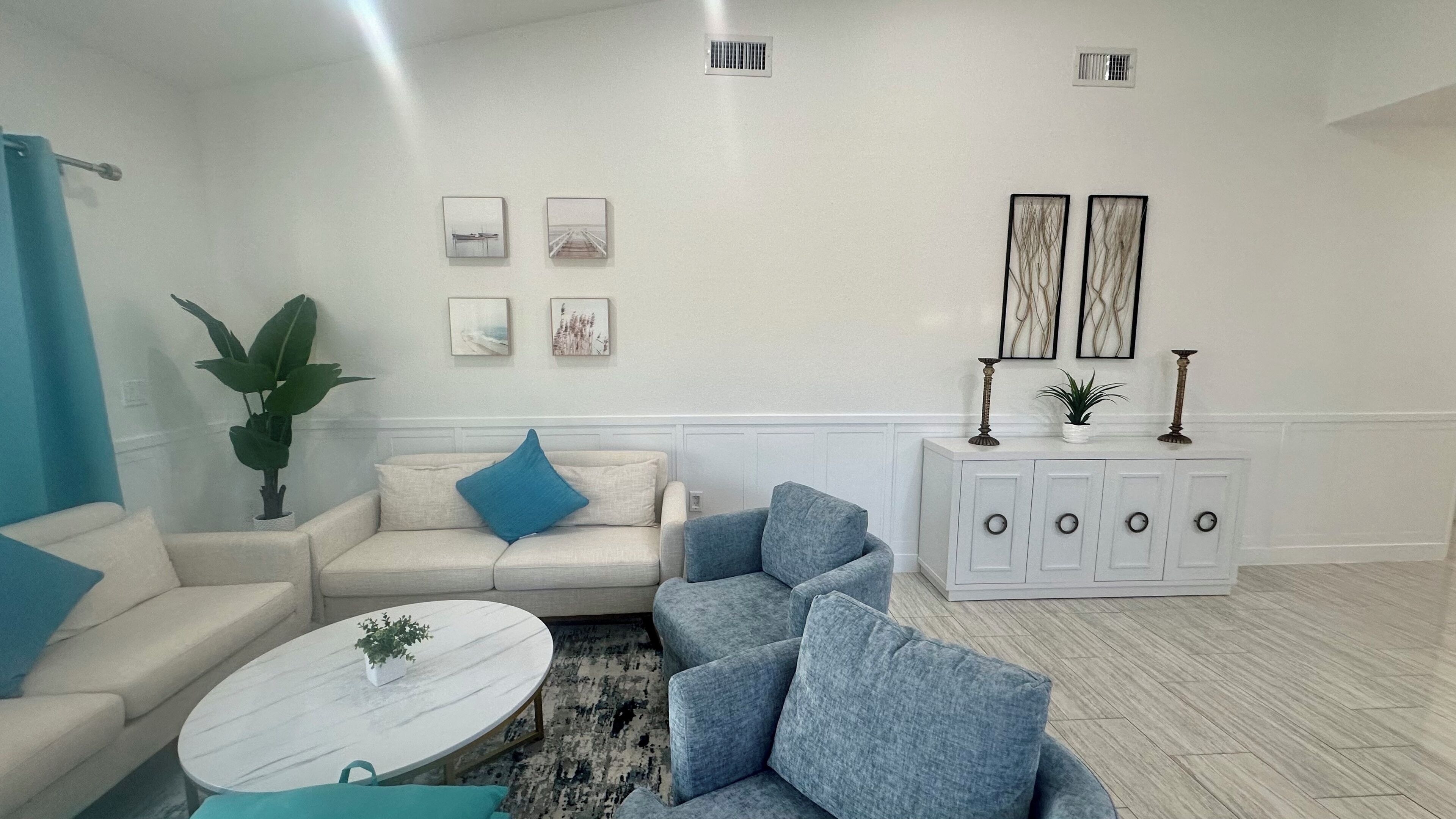 Ein Wohnzimmer mit einem beigen Sofa, einem blauen Sessel, einem weißen Couchtisch und einem weißen Schrank mit Dekorationselementen.