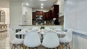 Une cuisine moderne avec des meubles en bois foncé, un comptoir en granit et un coin repas comprenant des chaises blanches et une table en marbre.