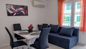Un salon moderne avec une table à manger blanche, des chaises noires, un canapé bleu foncé et un tableau accroché au mur.