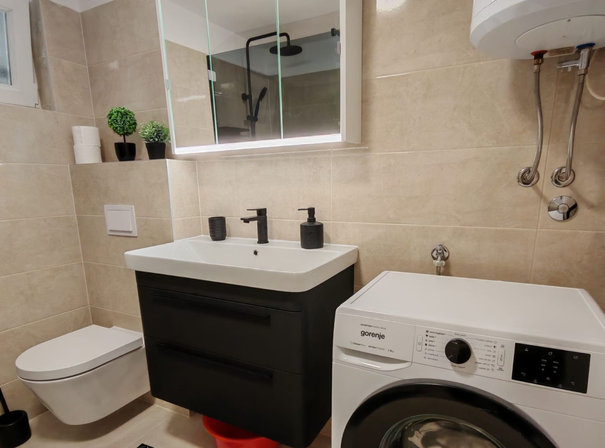 A modern bathroom with a toilet, sink, mirror, and washing machine.