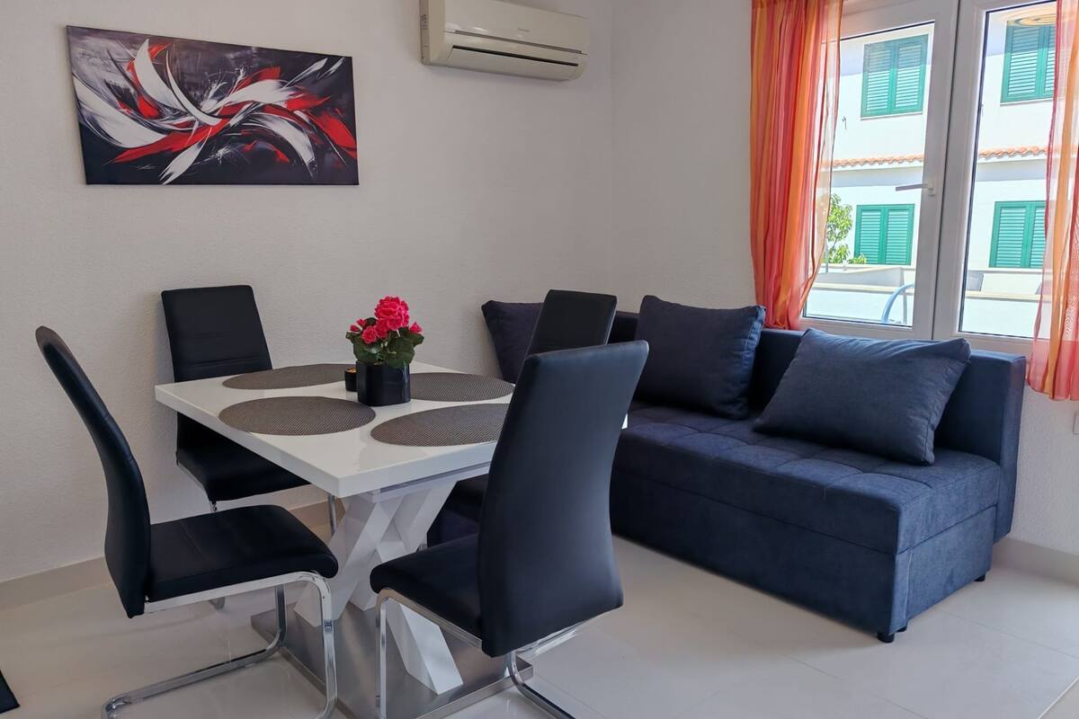 A modern living room with a sofa, chairs, a dining table, and a painting on the wall.