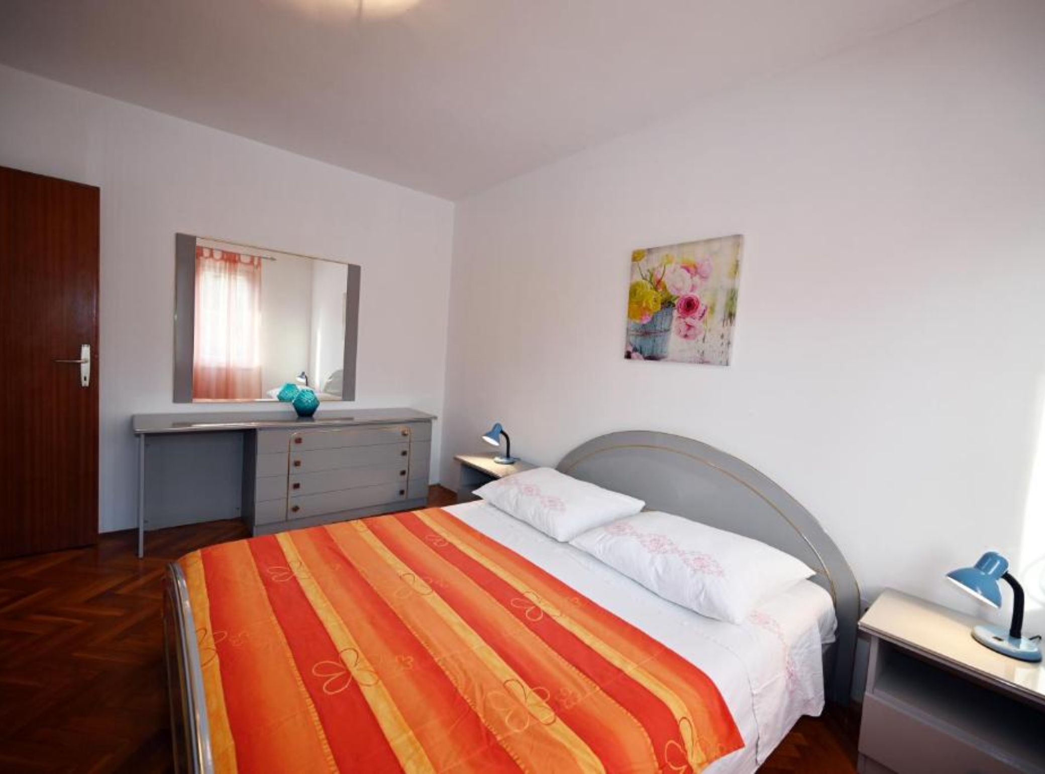 Un dormitorio con cama, cómoda, escritorio, silla, espejo y un cuadro en la pared.