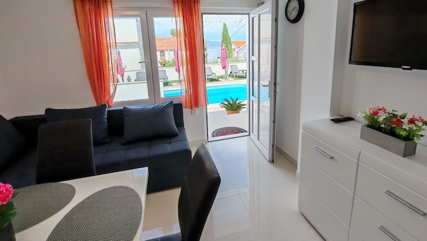 Un salon moderne comprenant un canapé, une table à manger, un téléviseur et donnant sur une piscine.