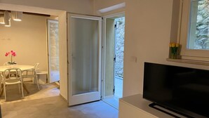 Una sala moderna con un televisor de pantalla plana, un comedor con mesa y sillas, y un ventanal corredero que da a un espacio exterior.