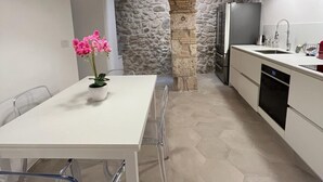 Una cocina moderna con armarios blancos, un arco de piedra y una zona de comedor con una mesa y sillas blancas.