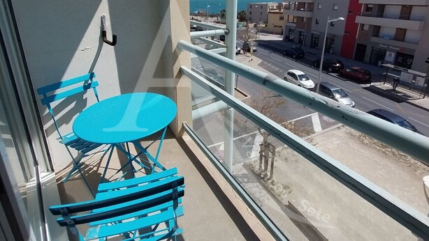 En balkon med et bord og stole, udsigt til gaden og bygninger i baggrunden.