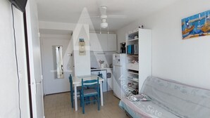 En kompakt opholdsstue med tekøkken, spiseplads med bord og stole samt en sofa.